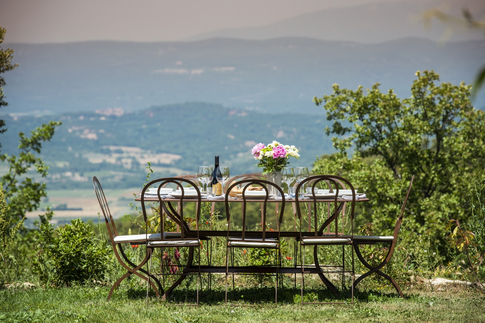 Outdoor dining area with set table, chairs, flowers and countryside view at Mas du Buis in Provence, France