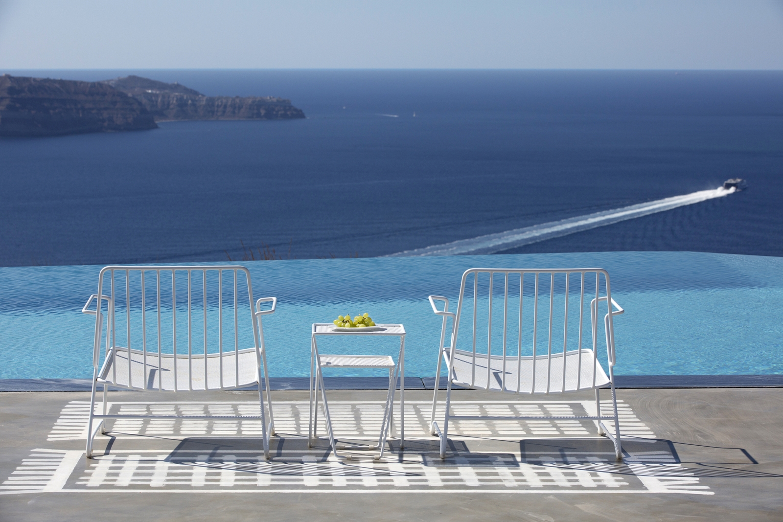 Chairs and coffee next to infinity pool on terrace with sea view at Erosantorini on Santorini, Greece