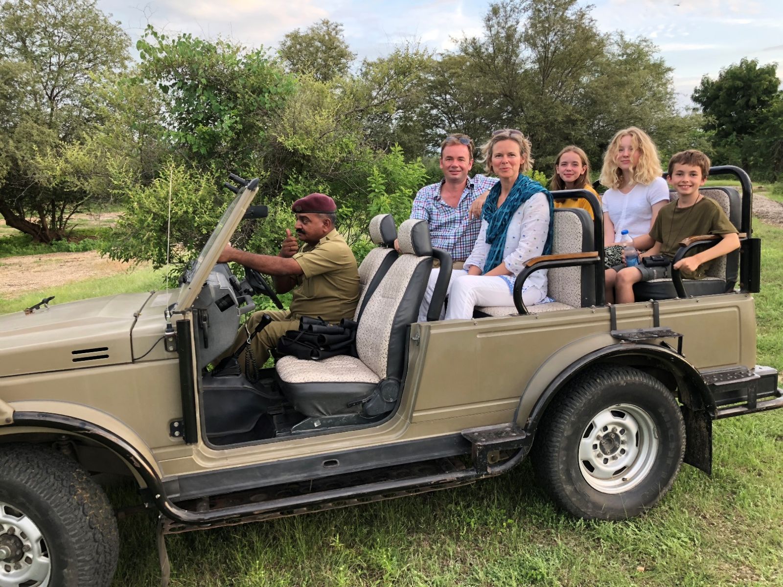 A family of two adults and three children sitting in a safari jeep with a driver in India