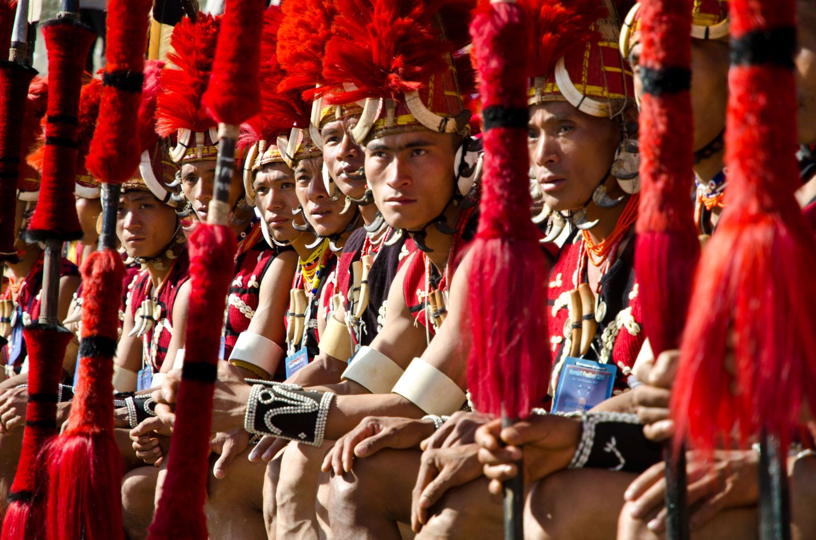 A row of men from the Tribes of Nagaland dressed in traditional red headdress and holding spears at the annual Hornbill Festival in India