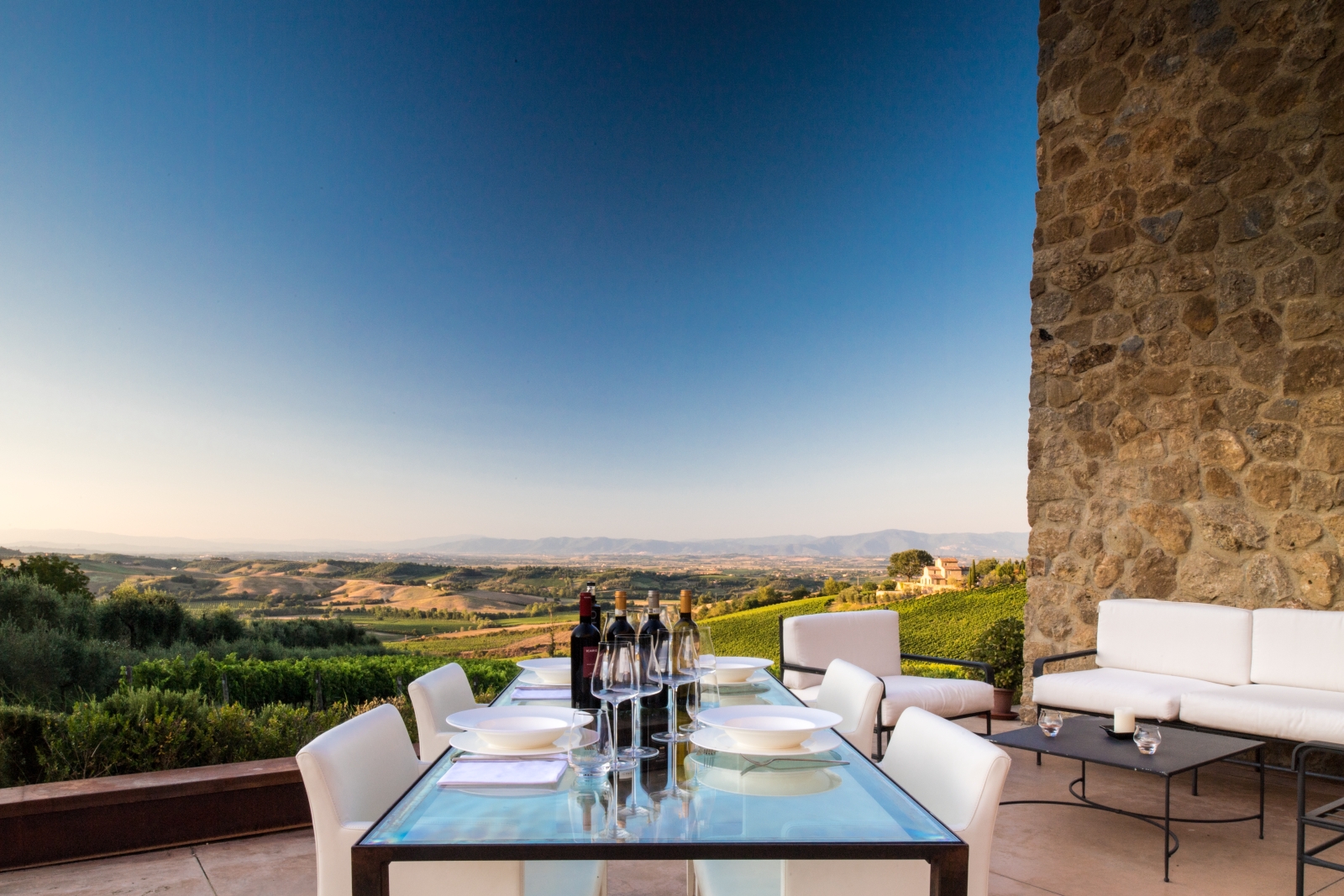 Terrace with dining table, wine, coffee table, sofas and countryside view at Villa dell’Angelo in Tuscany, Italy