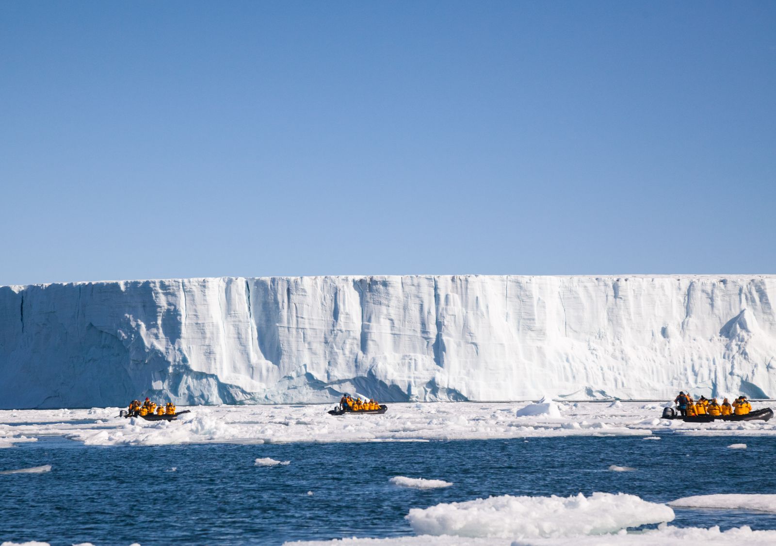 Three Zodiacs at the face of an enormous tabular iceberg in Svalbard Norway