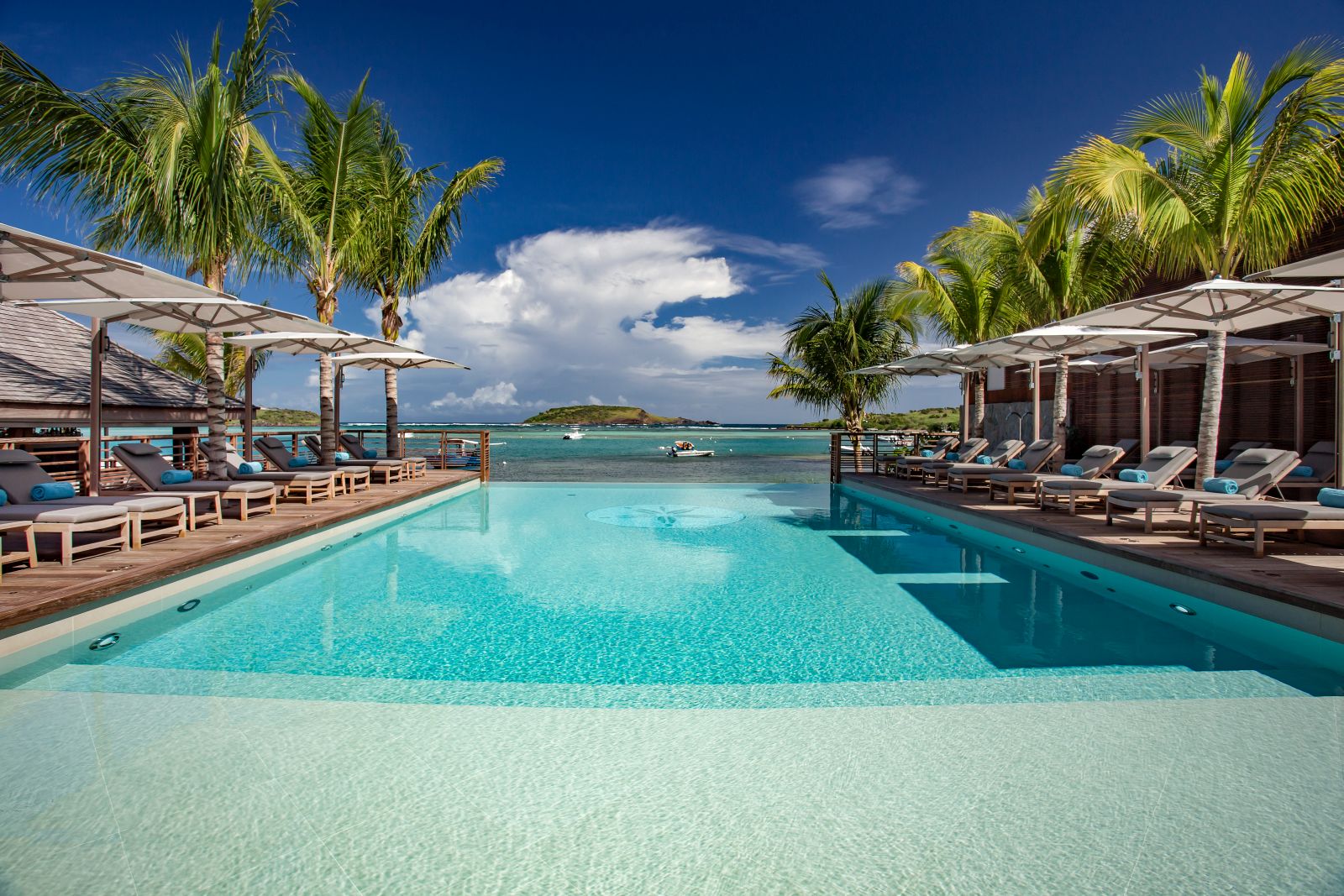 A view down the pool to the sea with sun beds and palm trees either side at Le Barthelemy Hotel & Spa in St Barths
