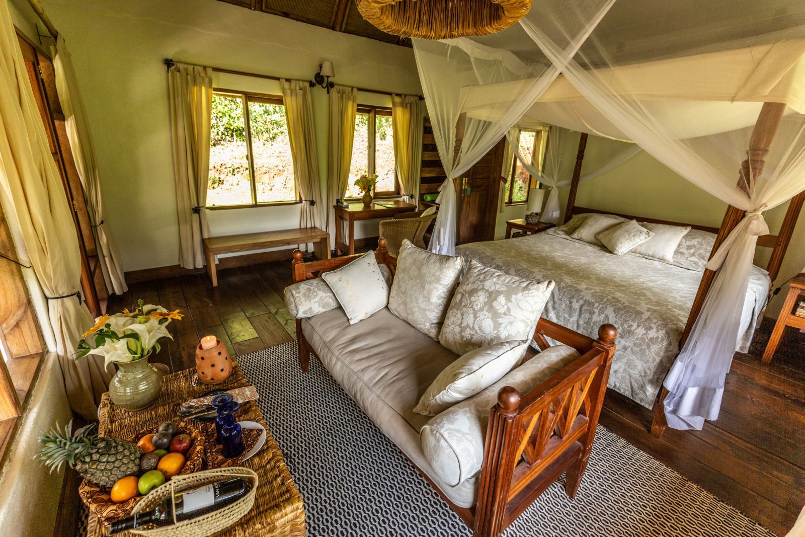 The living are in a bedroom at Bwindi Lodge in Uganda with a couch at the foot of a four poster bed. 