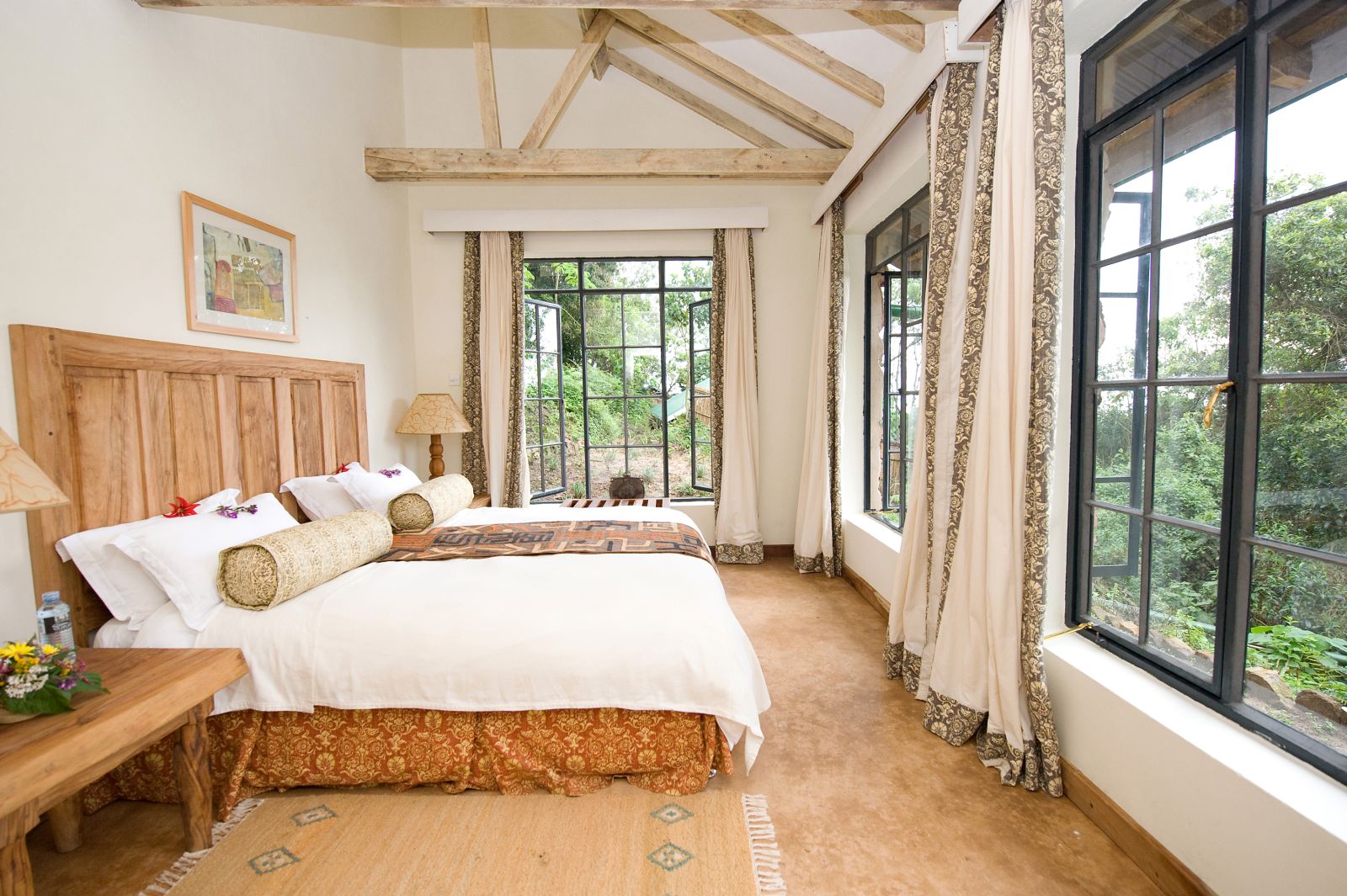 A bedroom with panoramic views from large windows at the foot of the bed at Clouds Mountain Gorilla Lodge in Uganda