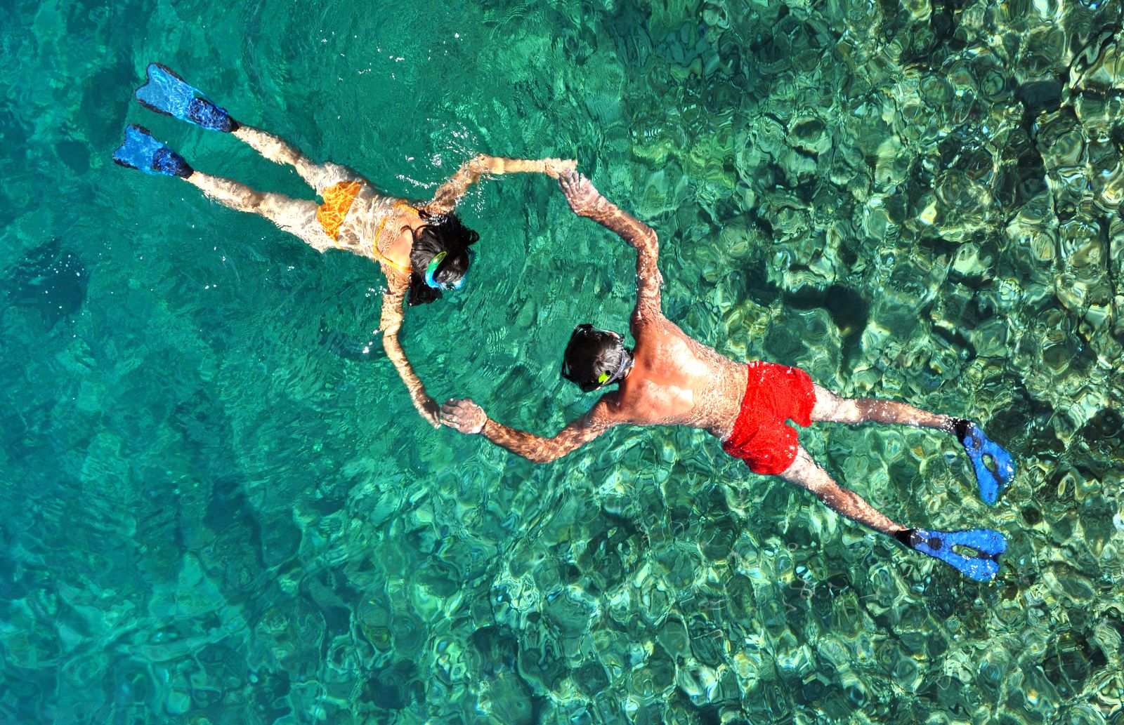 Aerial view of a couple holding hands while snorkelling in crystal-clear waters